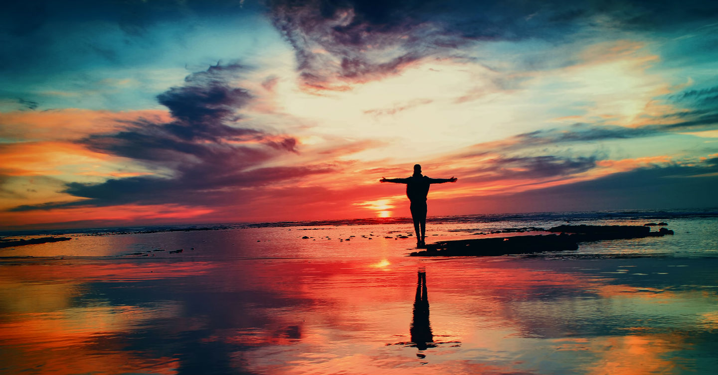 man standing on shore of sunset-lit beach