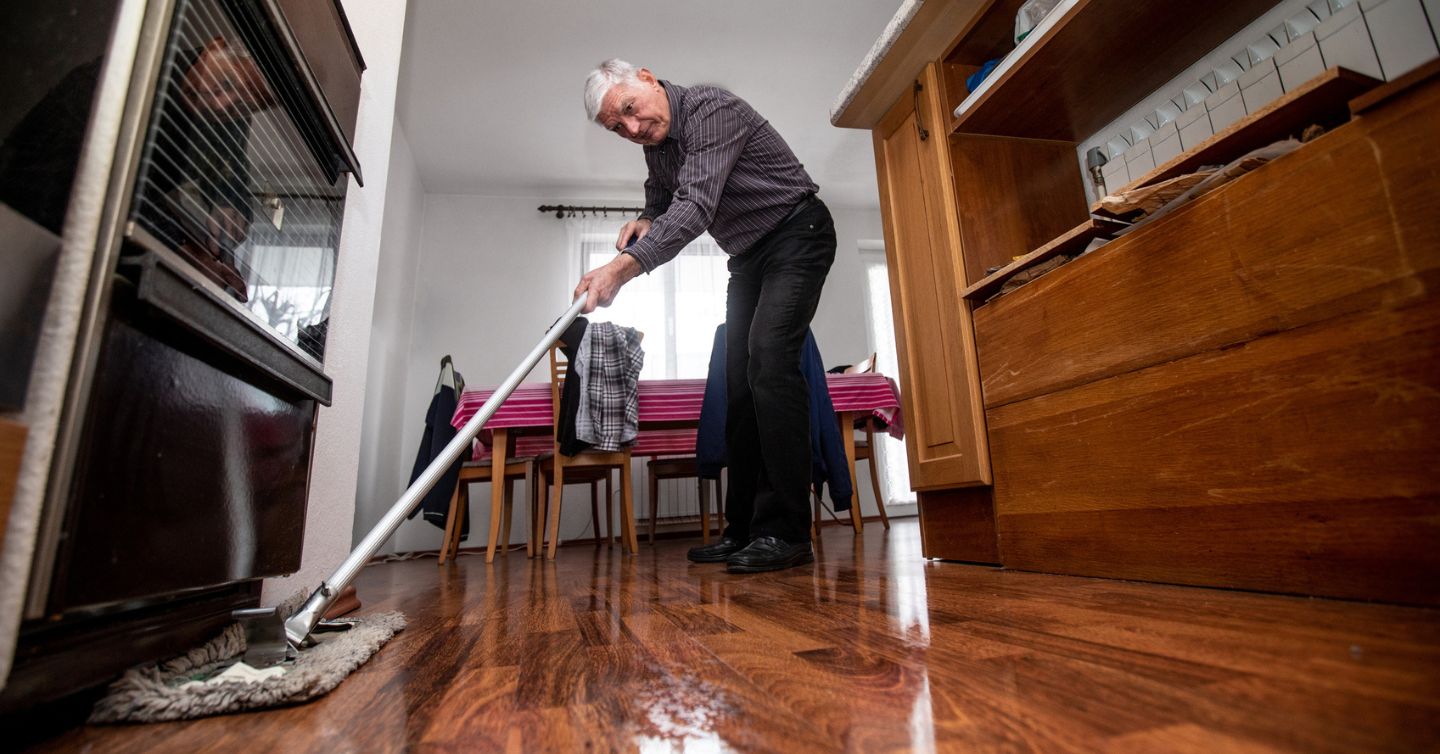 a senior man cleaning under his oven at home